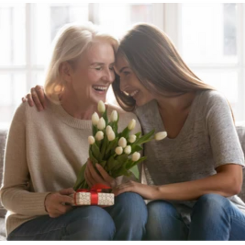 Gifts for gransparent.s Grand daughter is hugging grandmother and giving her flowers and a small gift. They both smiling and happy. 