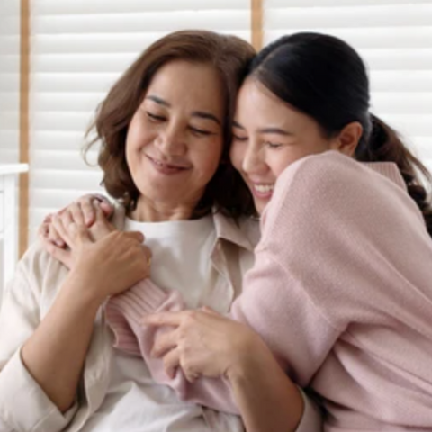 Daughter Gifting Mother.  Daughter is covering mother’s eyes with a present in front of her. Mother and daughter are happy and smiling.